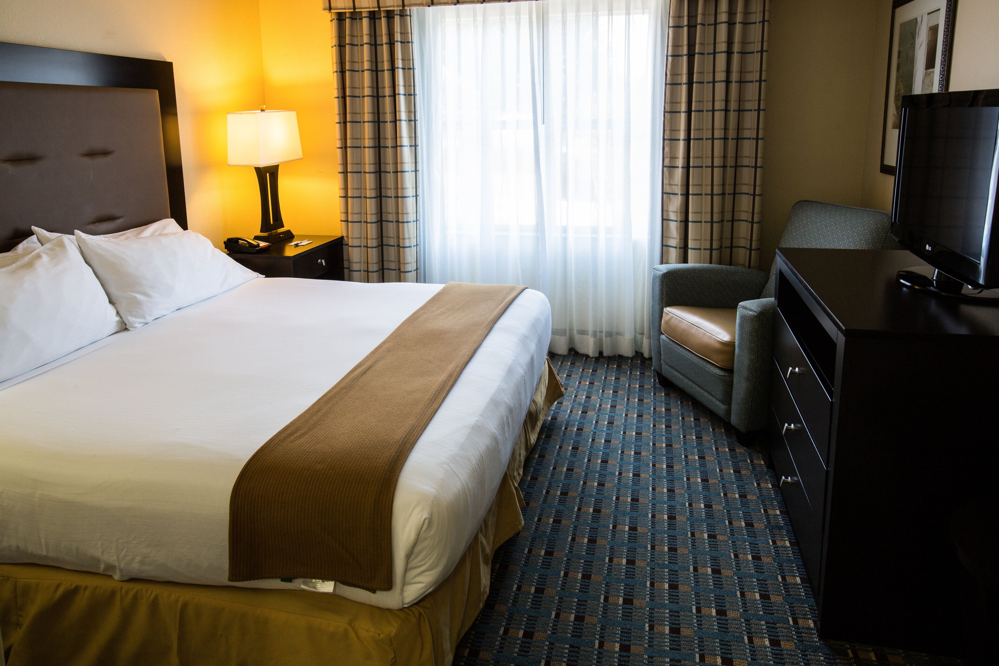 Ein Hotelzimmer mit einem großen Bett, einem Schreibtisch mit Fernseher, einem Sessel und einer Lampe.