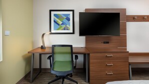 A hotel room with a wooden desk, a green mesh office chair, a flat-screen TV, and a framed abstract art piece on the wall. - Holiday Inn Express Alpharetta - Roswell by IHG (Alpharetta)