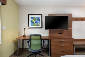 A hotel room with a wooden desk, a green mesh office chair, a flat-screen TV, and a framed abstract art piece on the wall. - Holiday Inn Express Alpharetta - Roswell by IHG (Alpharetta)