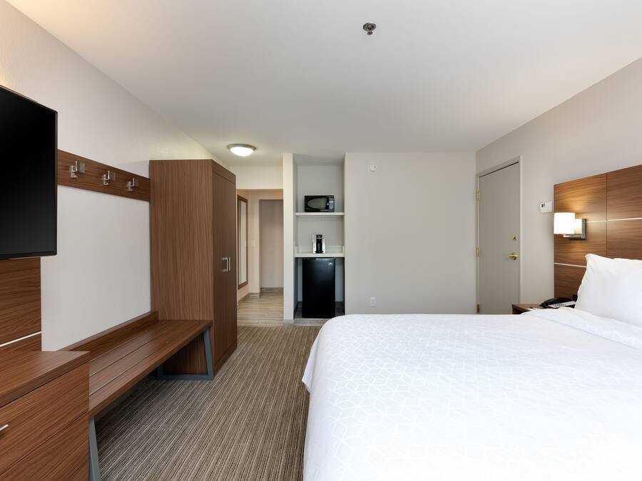 A hotel room with a bed, a TV, a desk, a wardrobe, a microwave, and a mini-fridge.