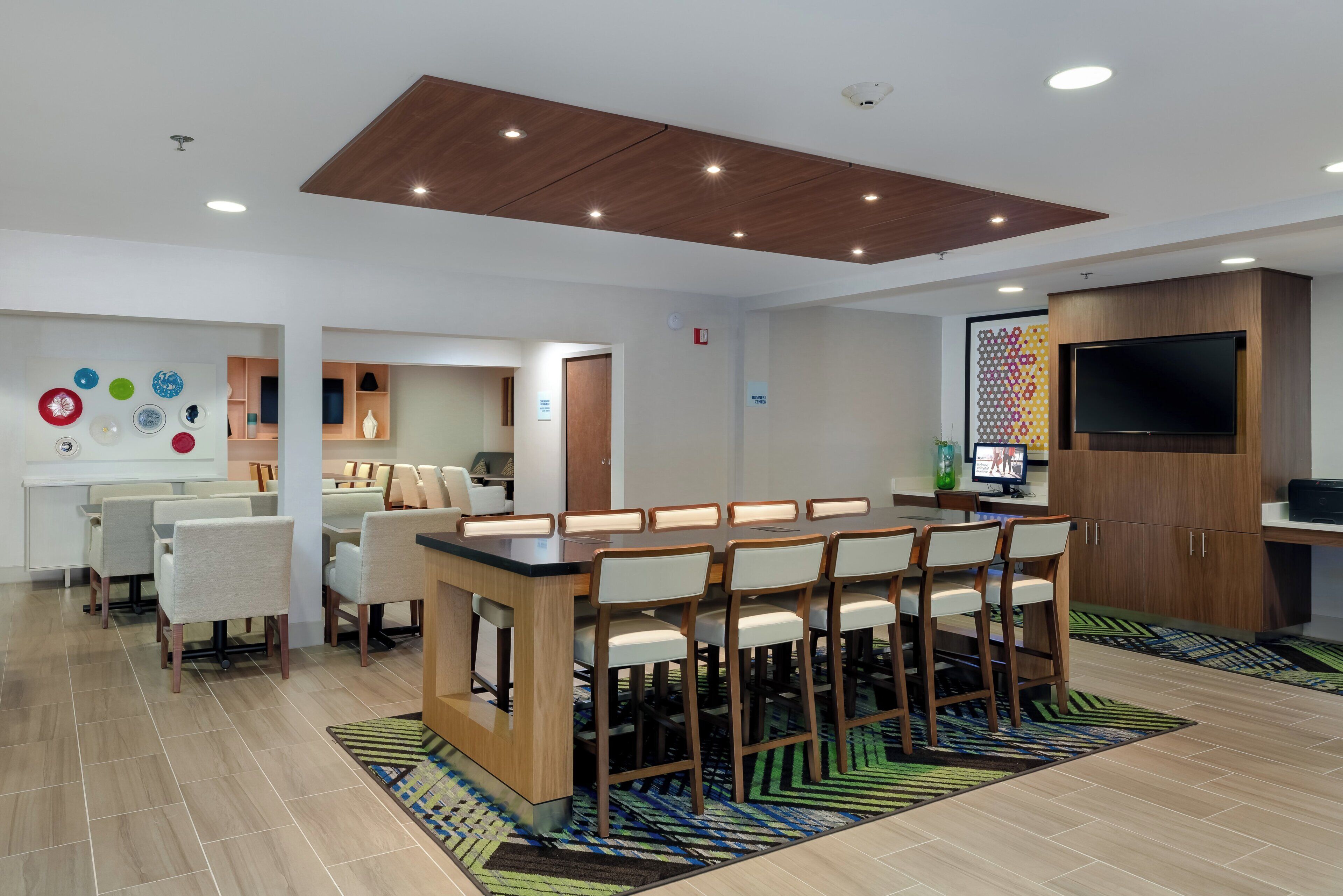 Une chambre d’hôtel moderne dotée d’un bar, de coins salon, d’un téléviseur à écran plat et d’un panneau indiquant l’emplacement du centre d’affaires.