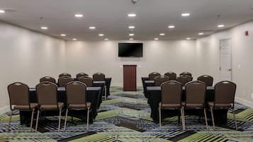 A conference room with a large screen, multiple tables, and chairs arranged for meetings.