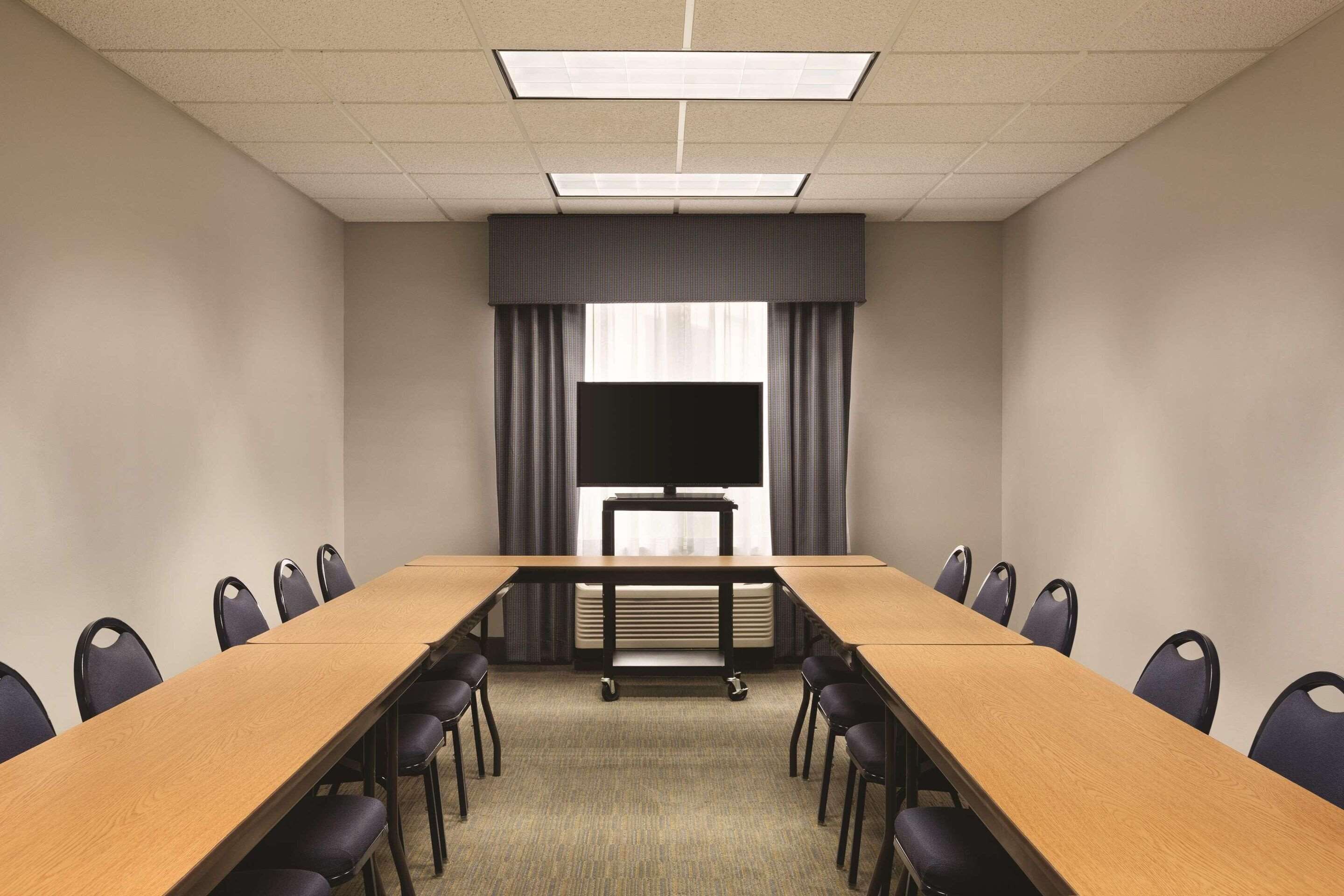 A conference room with a long table, chairs, a projector screen, and a large window with curtains.