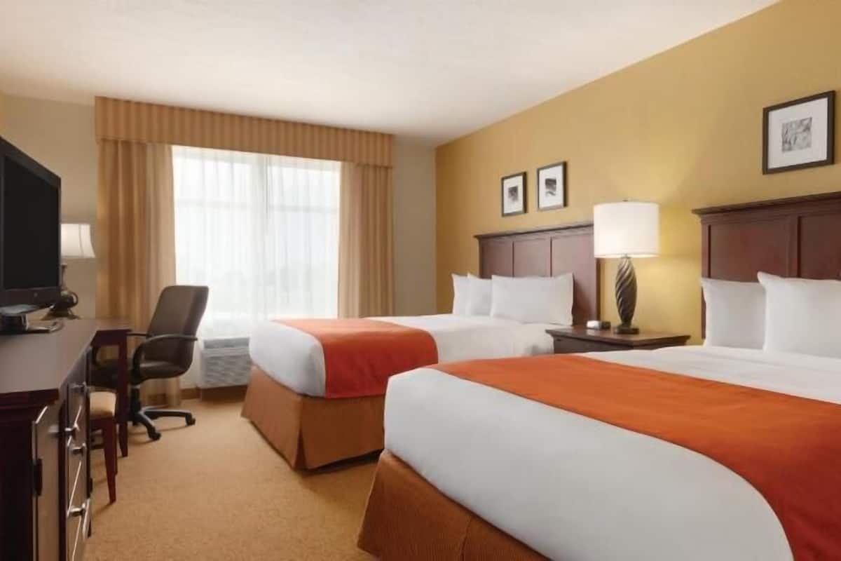 Habitación de hotel con dos camas, un escritorio, una silla, un televisor y cuadros en la pared.