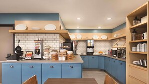 Een moderne keuken met blauwe kastjes, een houten eettafel en diverse keukenapparaten.
