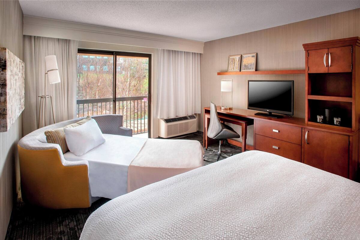 A hotel room with a large bed, a desk with a TV, a chair, and a wardrobe.