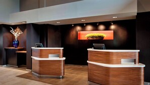 A reception area with two wooden reception desks, a vase with branches, and a wall-mounted display. - Courtyard by Marriott Parsippany (Parsippany)