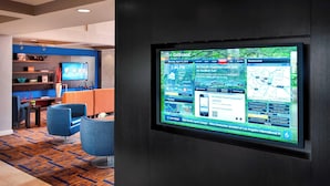 A hotel lobby with a large digital screen displaying news and travel information. There are seating areas with blue chairs and a patterned carpet. - Courtyard by Marriott Parsippany (Parsippany)