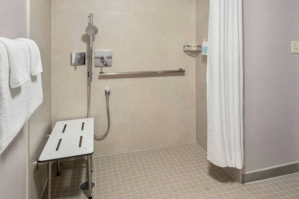 A modern shower area with a handheld showerhead, a handheld shower attachment, and a grab bar.