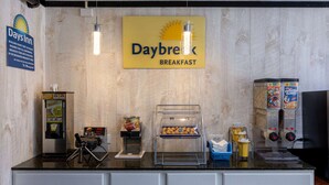 A breakfast counter with a sign reading "Daybreak Breakfast," a coffee machine, a syrup dispenser, and a display of cereal boxes. - Days Inn by Wyndham Columbia (Columbia)