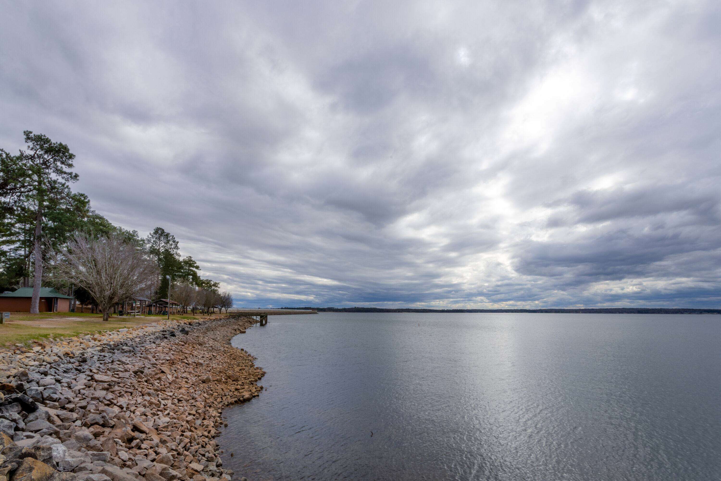 Un lac paisible, bordé d’une rive rocheuse et d’une rangée d’arbres.
