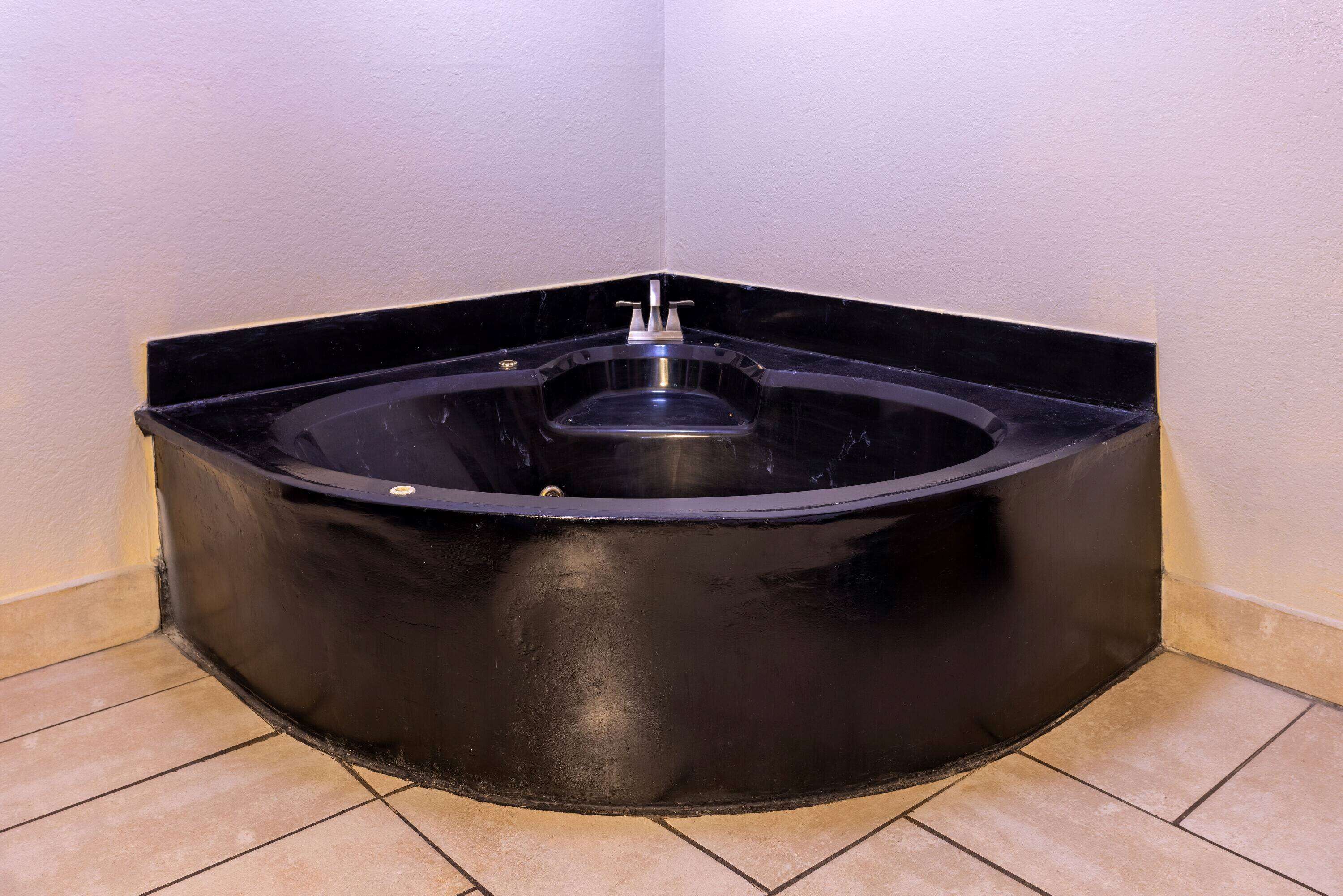 Une baignoire d’angle avec un revêtement noir, un robinet et un drain.