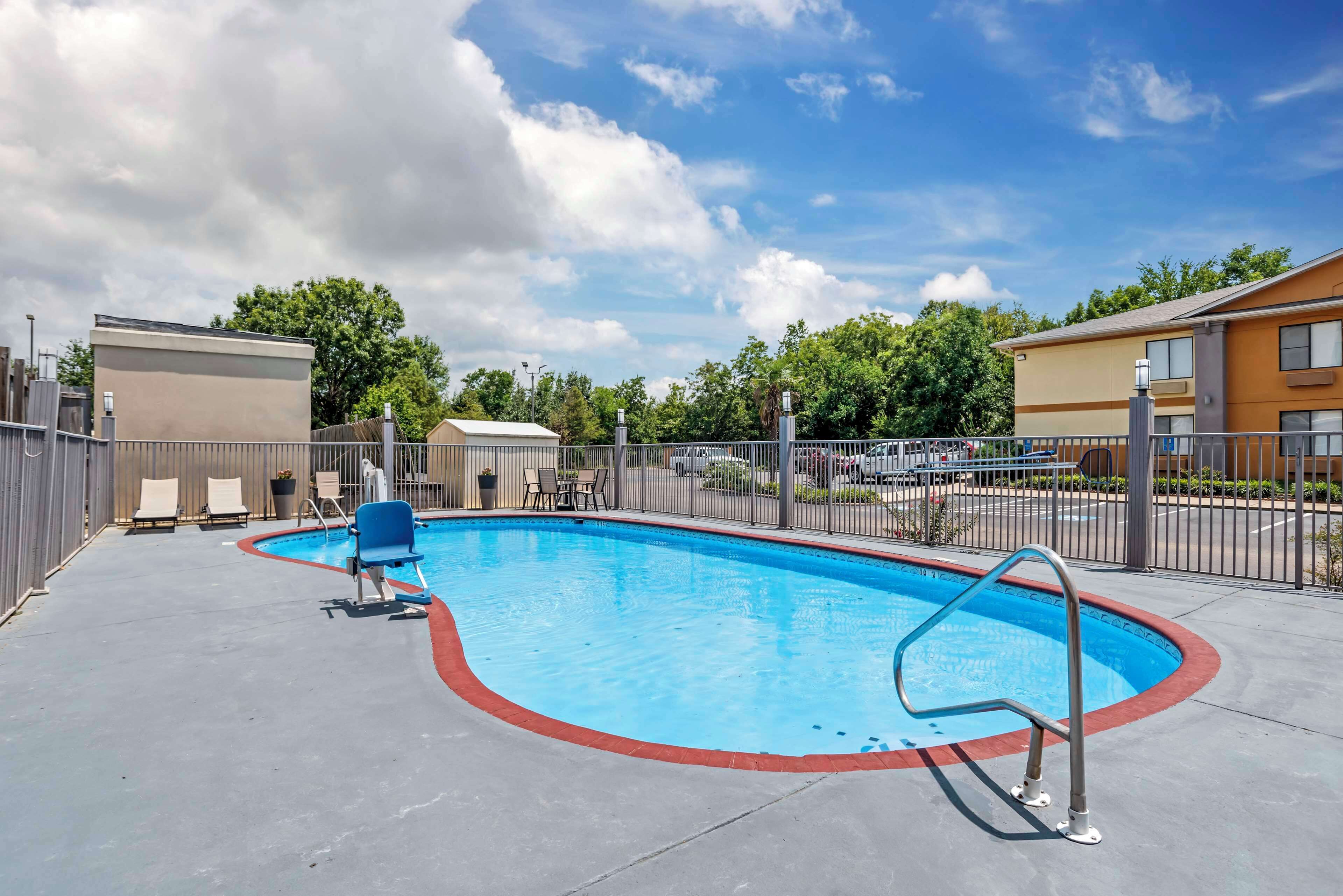 Ein Swimmingpool mit Metallleiter, umgeben von einem Zaun und einigen Liegestühlen.