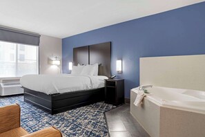 A hotel room with a bed, bedside table, lamp, and a large bathtub.