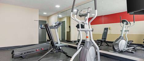 Un gimnasio con cintas de correr, elípticas y un espejo grande.