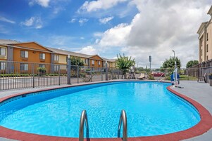 A swimming pool with metal railings, surrounded by a fence, and adjacent to residential buildings.