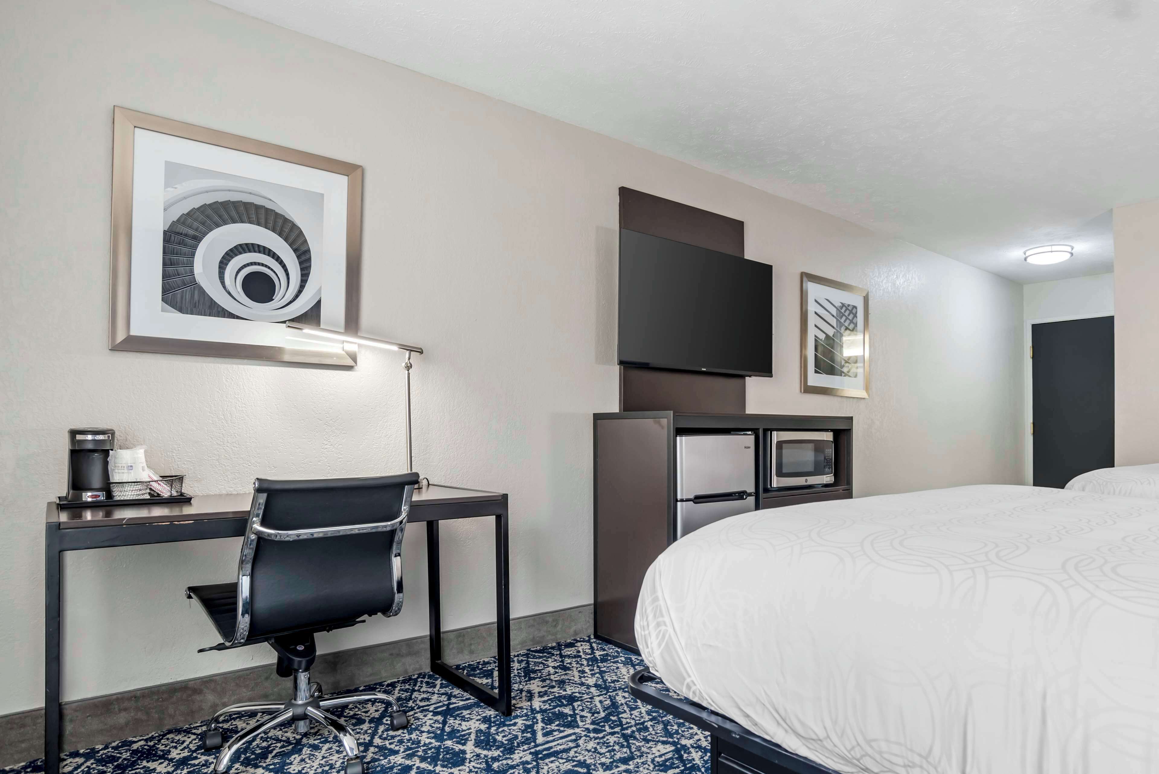 Habitación de hotel con cama, escritorio con silla, televisor de pantalla plana, microondas y refrigerador.