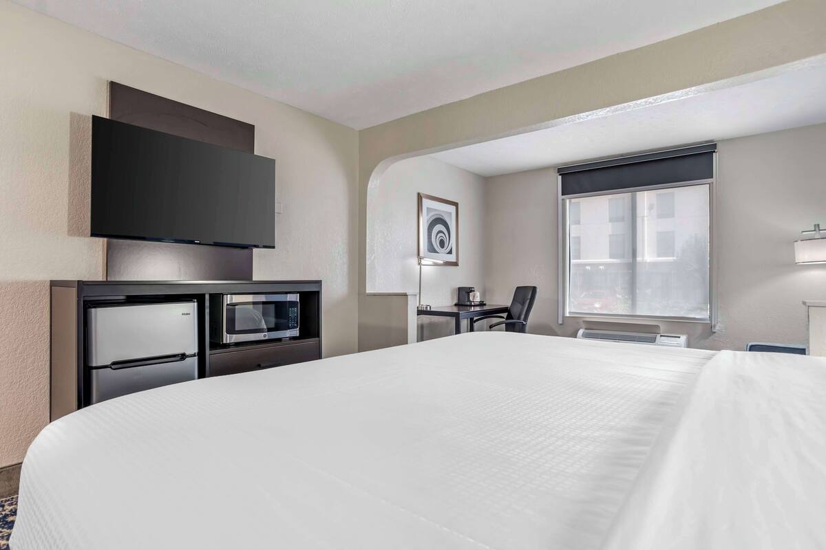 A hotel room with a large bed, a flat-screen TV, a microwave, a desk, and a chair.