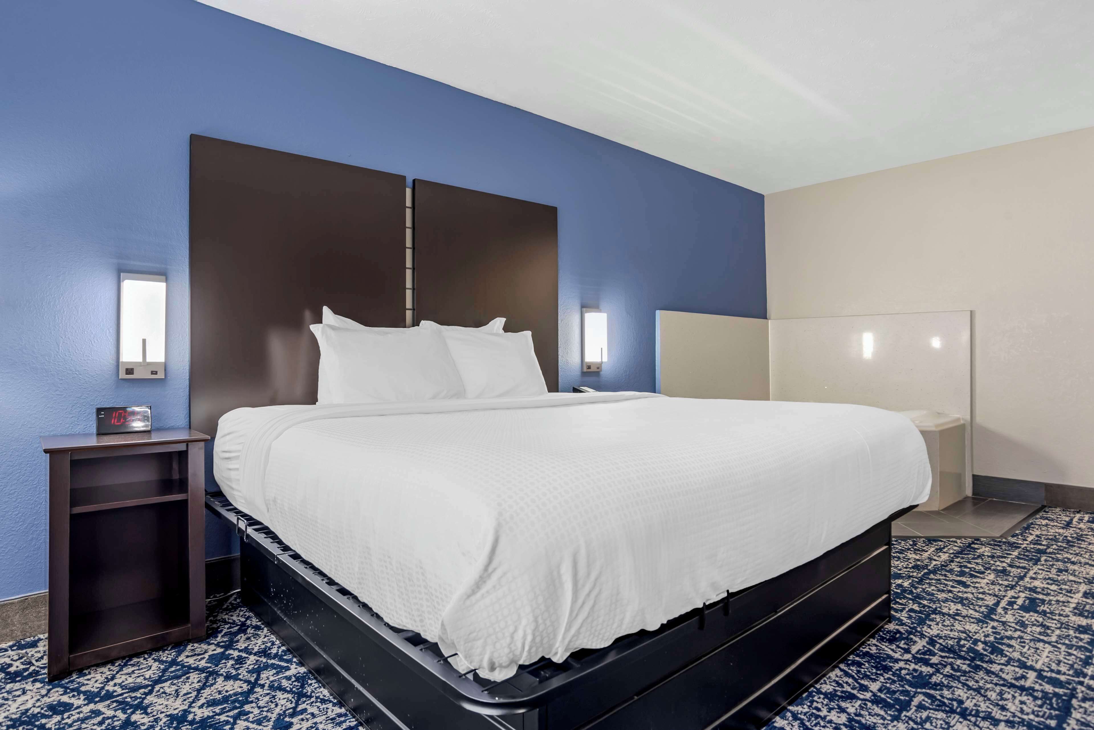Une chambre d’hôtel avec un grand lit, une table de chevet et une lampe fixée au mur.