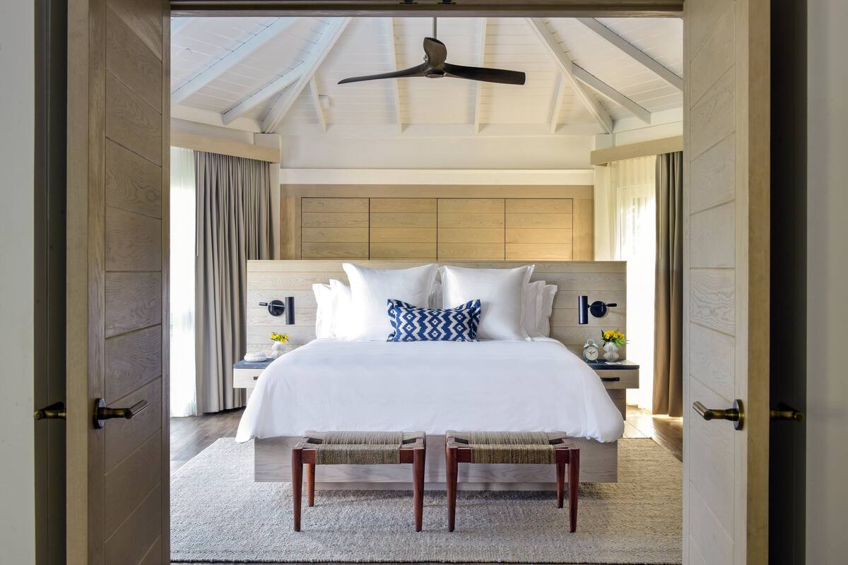 Une chambre avec un grand lit, une tête de lit en bois, des tables de chevet et un ventilateur de plafond.