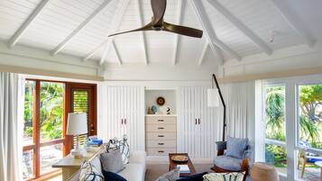 A spacious living room with a ceiling fan, a sofa, a coffee table, and a chair. There is a window with a view of greenery outside.