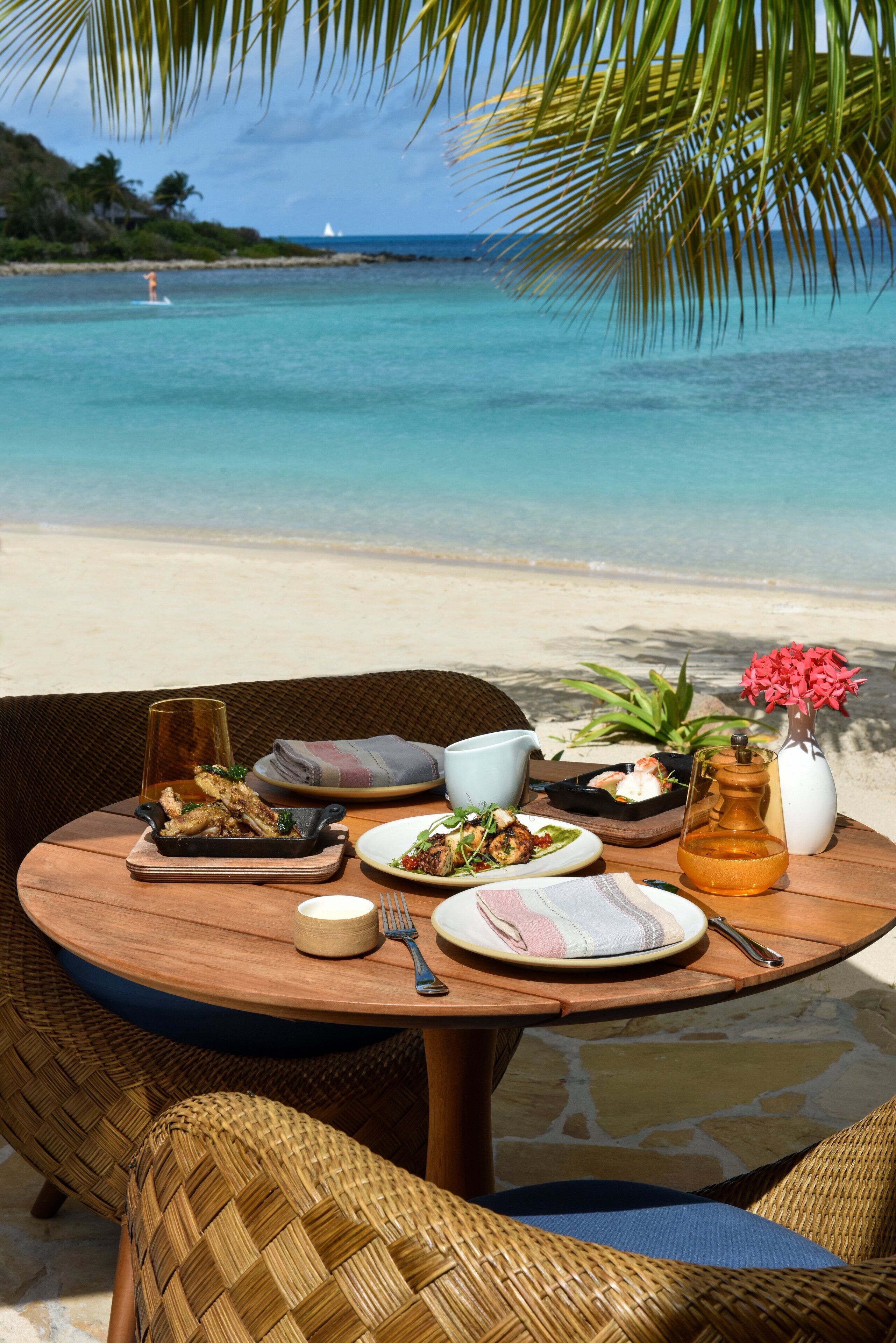 Une table dressée avec différents plats et boissons, placée sur une plage donnant sur l’océan.