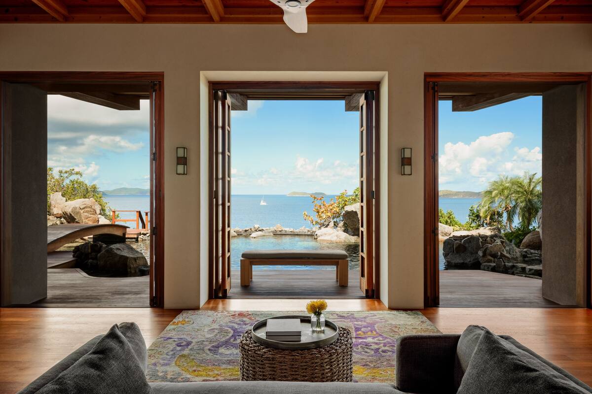 Une pièce spacieuse avec un plafond en bois et une grande fenêtre donnant sur une piscine et la mer.