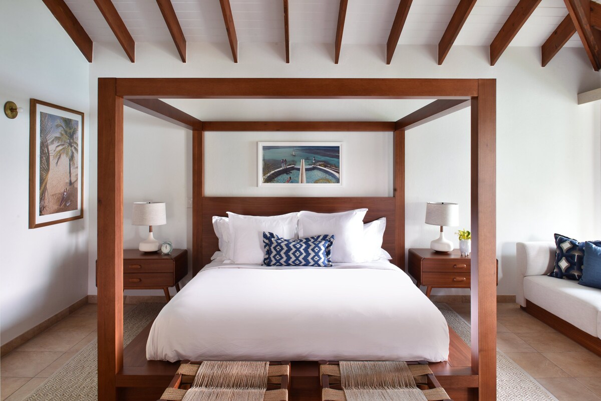 A four-poster bed with white bedding, two nightstands with lamps, and a framed picture above the bed.
