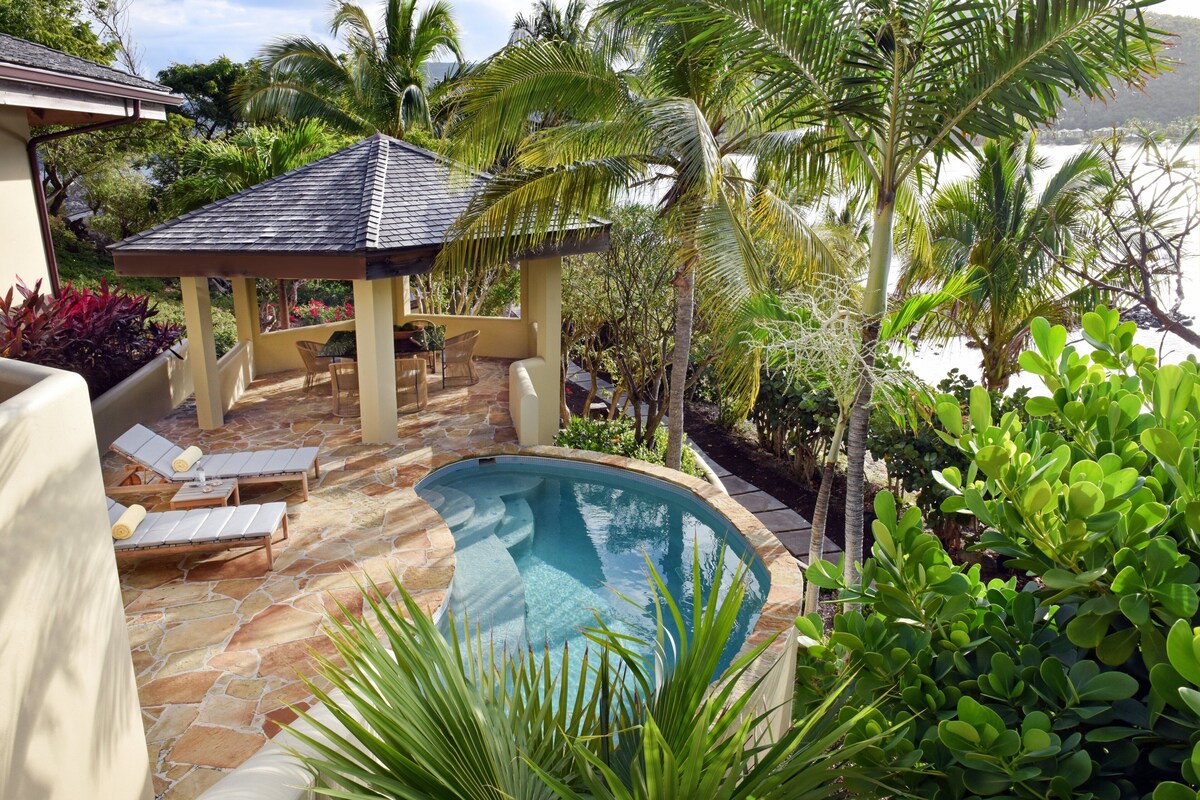 A pool area with lounge chairs, a gazebo, and tropical plants.