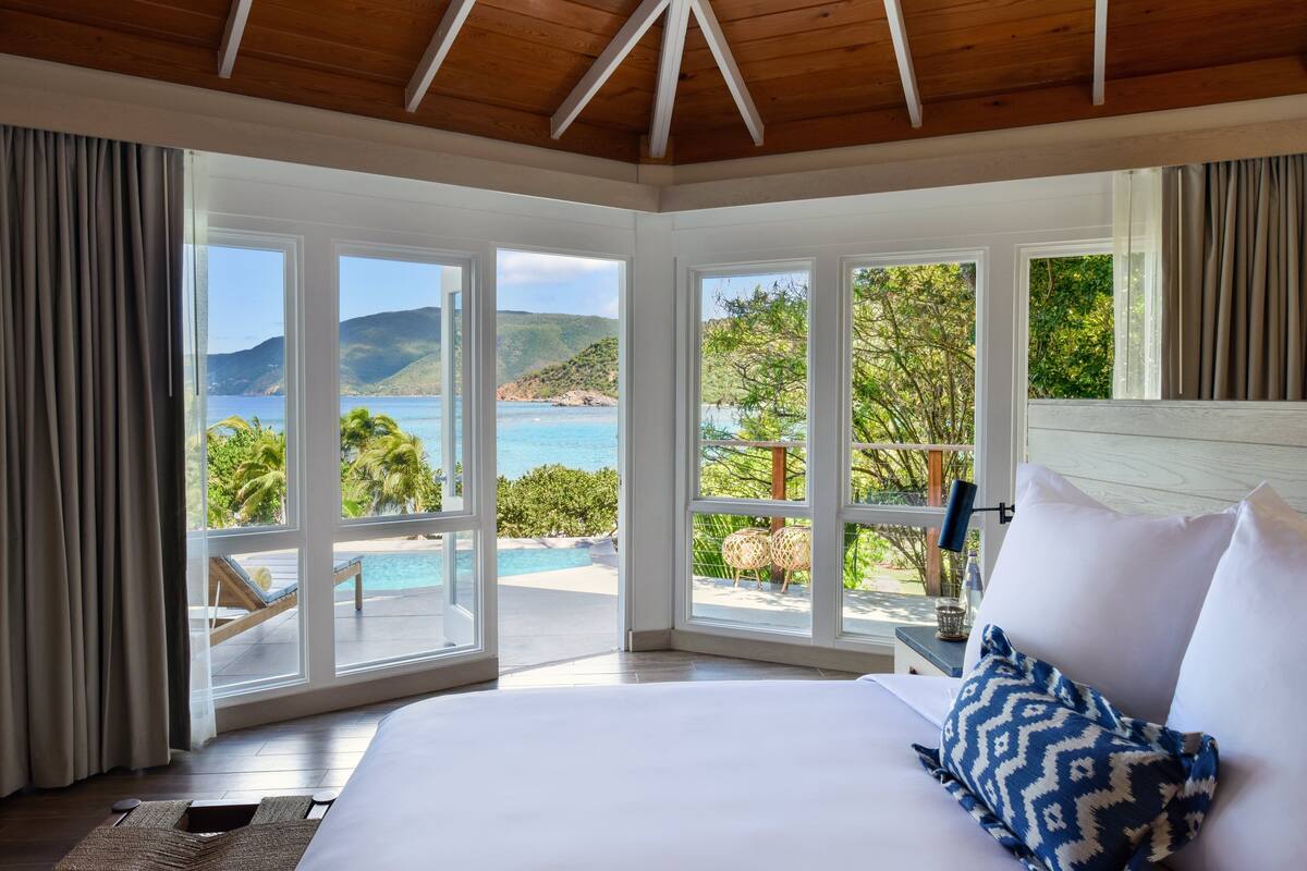 Une chambre avec un grand lit, une vue sur la mer et un balcon équipé de chaises longues.