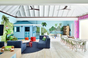 A room with a blue and white color scheme, featuring a sofa, a dining table with chairs, and a ceiling fan.
