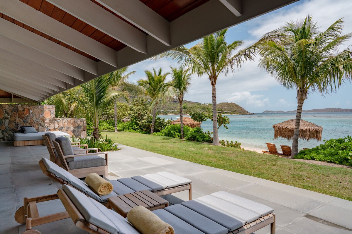A covered outdoor seating area with lounge chairs and a stone wall.