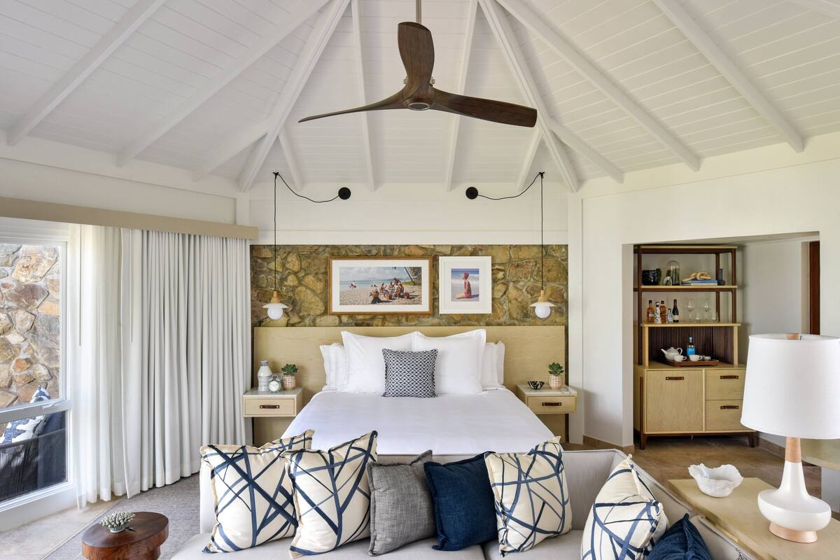 Une chambre spacieuse avec un grand lit, un ventilateur de plafond, un mur en pierre et une vue sur l’extérieur.