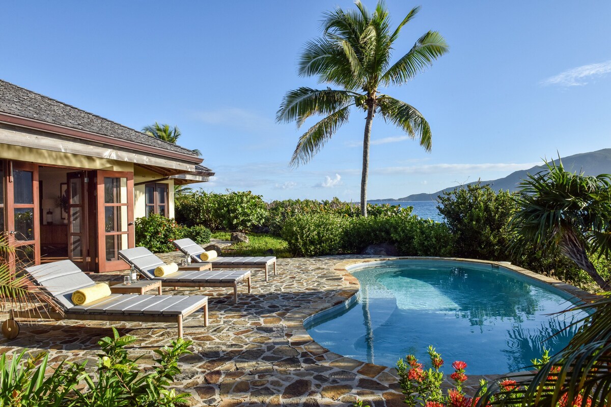 A pool area with lounge chairs, a stone deck, and a view of the ocean.