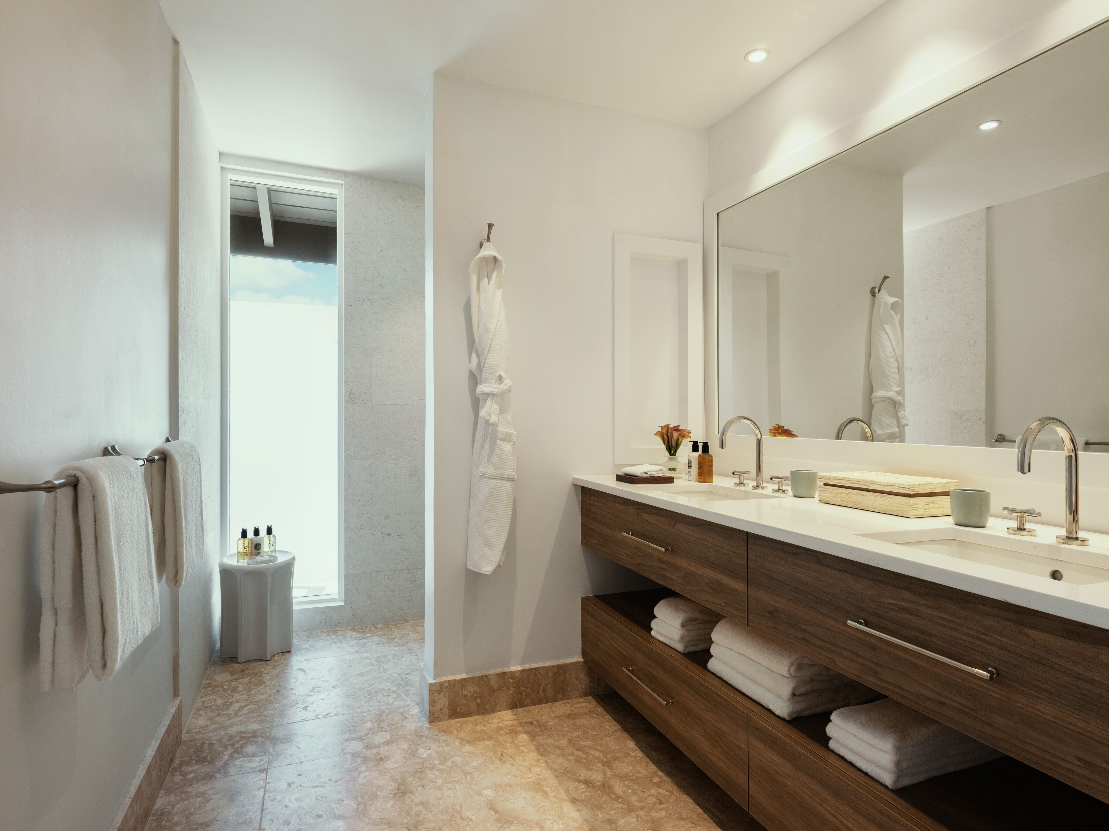 A modern bathroom with a large mirror, dual sinks, and a vanity with storage drawers.