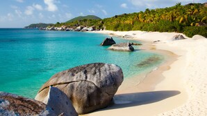 Una playa con agua turquesa cristalina, rocas grandes y arena blanca.