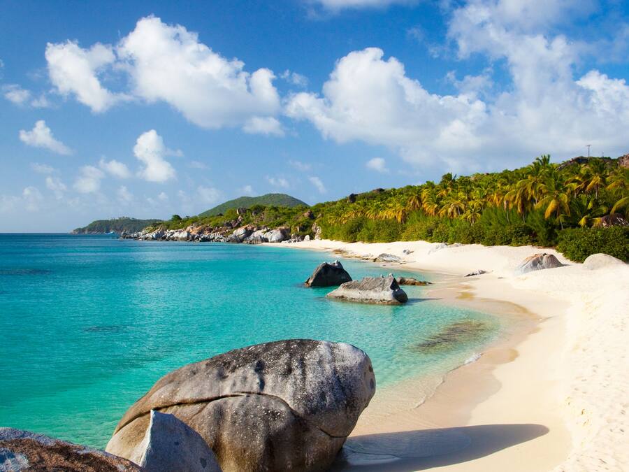 A beach with clear turquoise water, large rocks, and white sand.