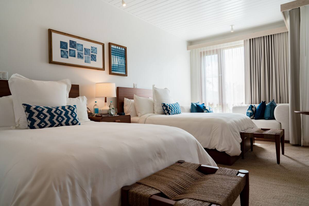Une chambre d’hôtel avec deux lits, un coin salon et une grande fenêtre avec des rideaux.