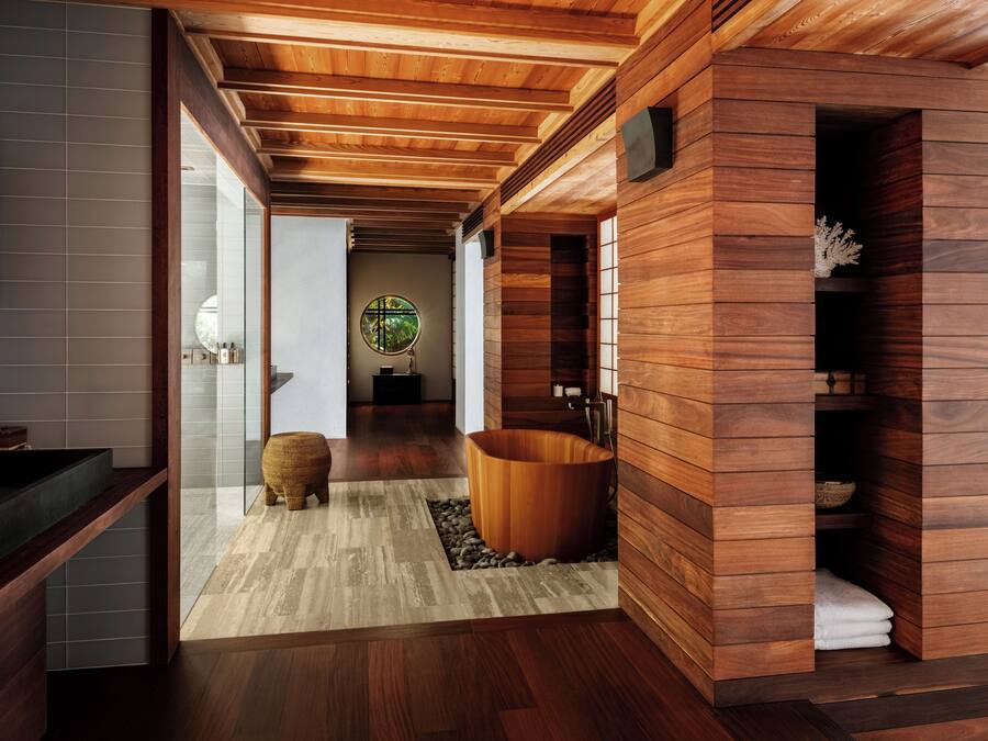 A modern bathroom with wooden paneling, a large bathtub, and a round mirror with a tropical view.
