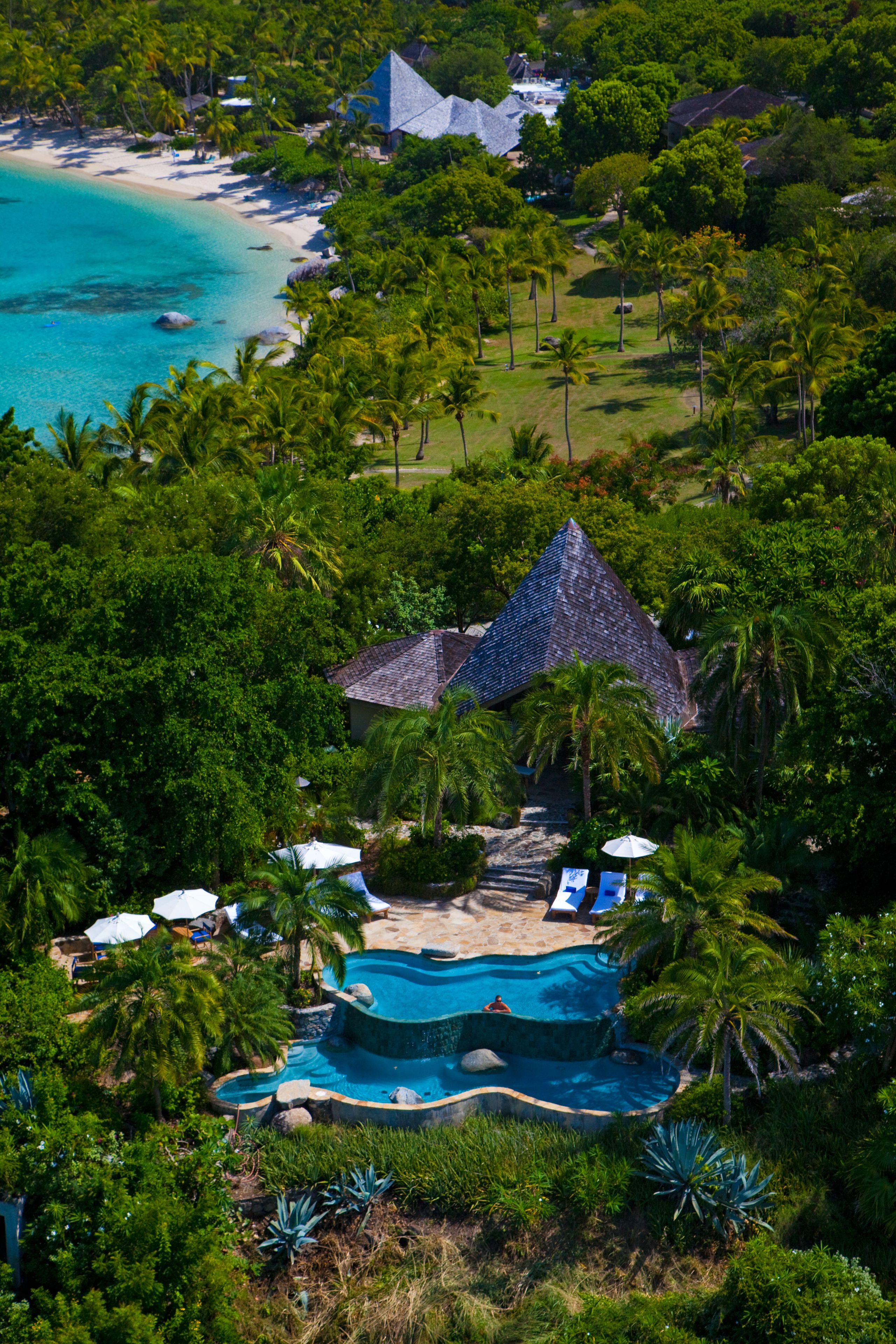 Vue aérienne d’un complexe hôtelier doté d’une piscine, d’une plage et d’une végétation luxuriante.