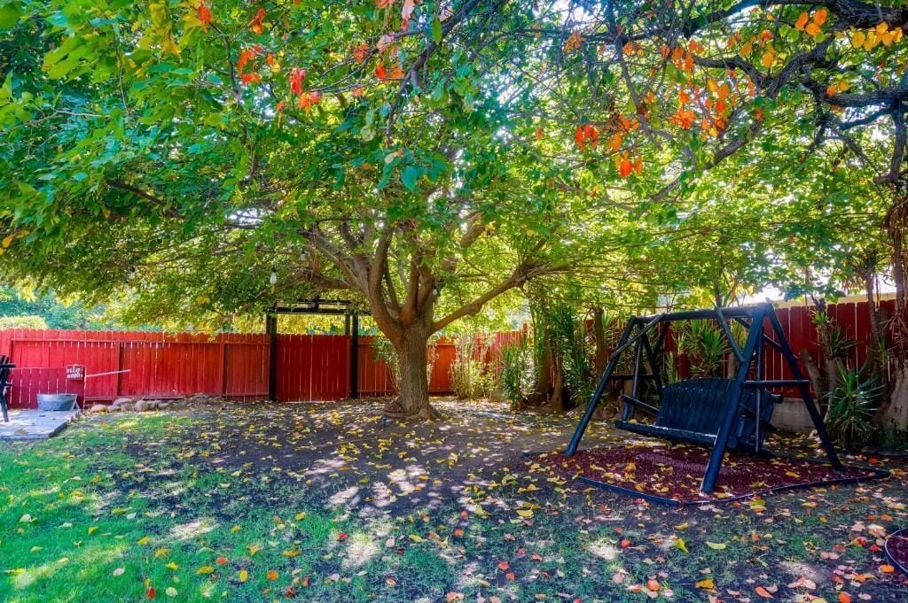Un patio trasero con un columpio, un árbol y una cerca roja.