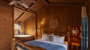 A wooden cabin bedroom with a bed, a nightstand, a wall-mounted lamp, and a wooden headboard.