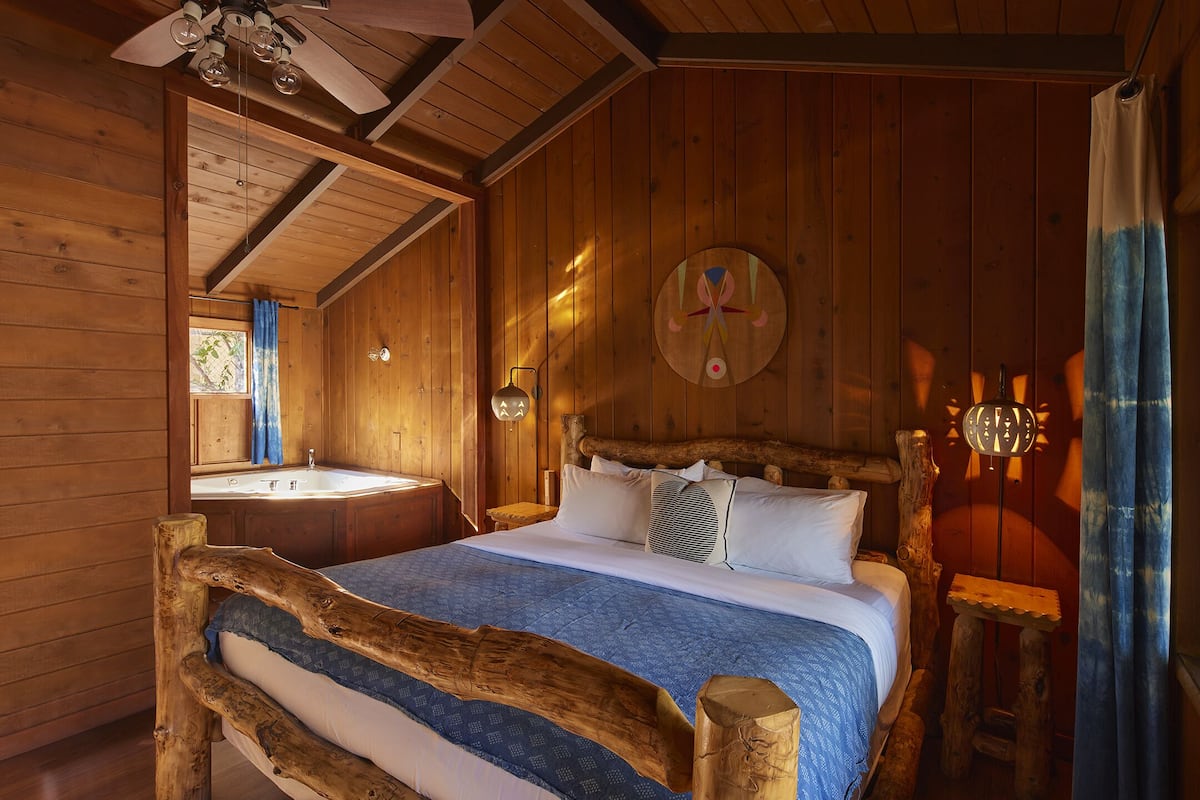 A wooden cabin bedroom with a bed, a nightstand, a wall-mounted lamp, and a wooden headboard.