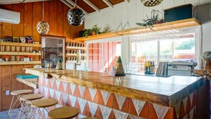 A bar area with a wooden counter, stools, and shelves with bottles and glasses.