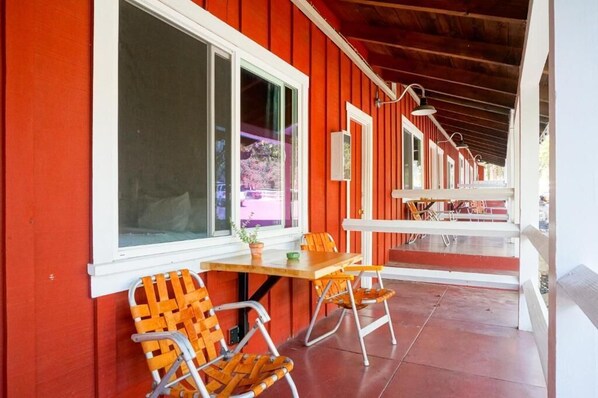 A red building with a covered porch, a table with chairs, and a window with a view of a pink building.