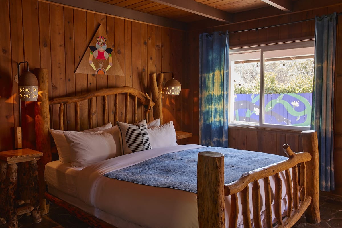 A wooden cabin-style bedroom with a bed, wooden headboard, and a window with curtains.