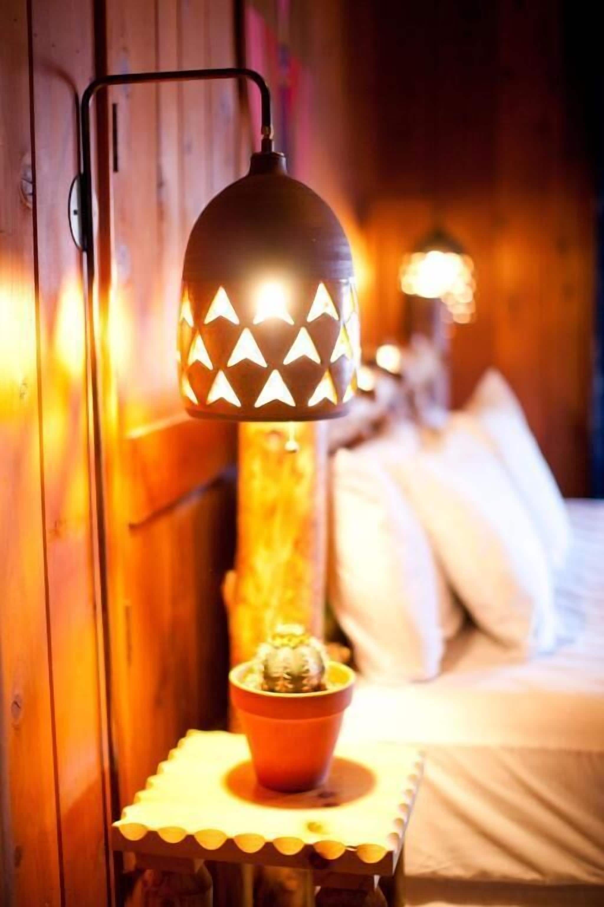 A cozy room with a bed, a small table with a bowl, and a wall-mounted lamp.
