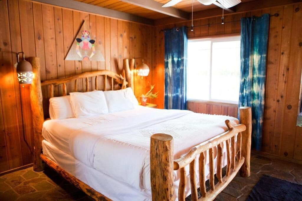 A wooden room with a bed, wooden walls, and a window with curtains.