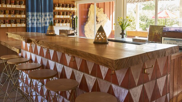 A bar area with a wooden counter, stools, hanging pendant lights, and a view of the outdoors.