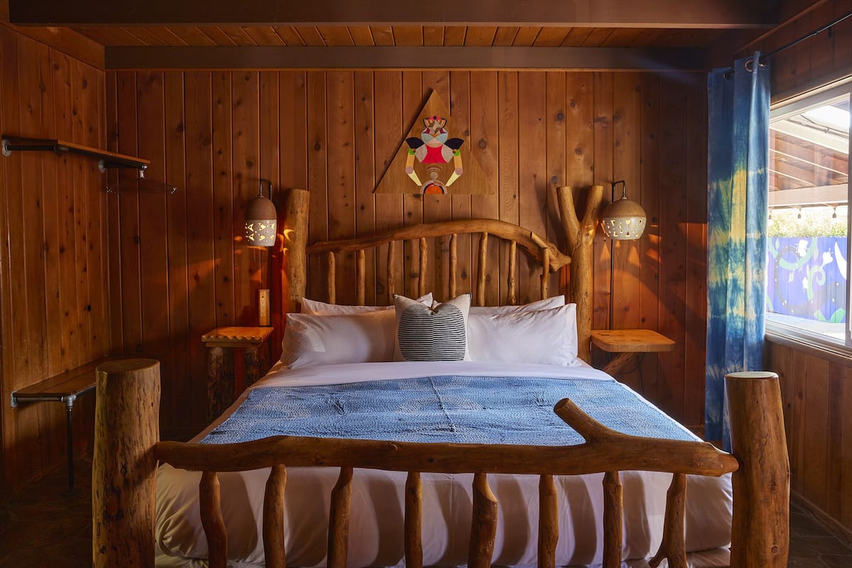 A wooden cabin room with a bed, wooden headboard, and two wall-mounted lamps.